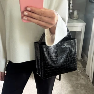 Svart handväska  - Säljer denna handväska som aldrig kommit till användning, väskan är som ny 🥰långt band medföljer, innerfack  Mått: bredd 25, höjd 20 