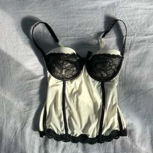 Vit korsett med svarta detaljer - Jättefin vit korsett från Sensuality med svart boning och blomdetaljer. Den är i fint skick. Tyget är lite stretchigt och både axelband och rygg går att justera. Därför passar den nog många. Skriv gärna om du undrar något eller vill ha fler bilder!<3