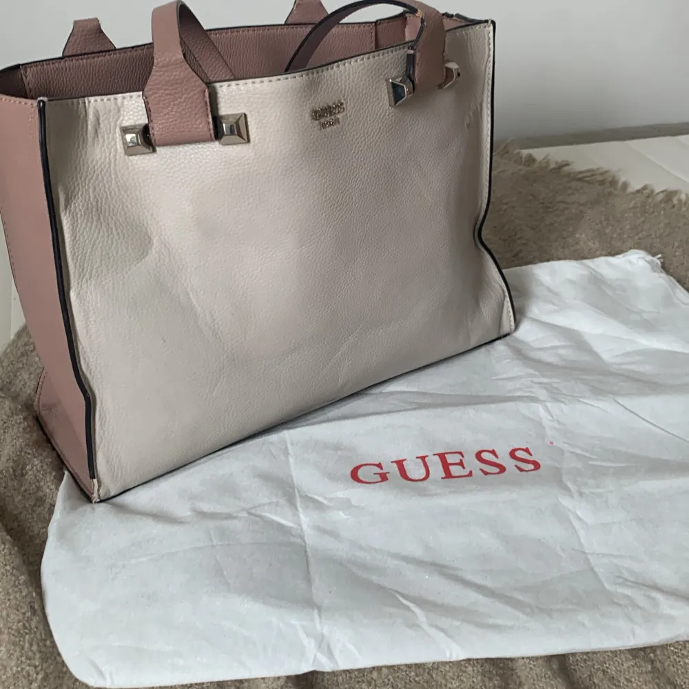 En handväska från Guess i beige brun färg. Väskan har två handtag och en rymlig insida med flera fack. Den är tillverkad i skinn och har Guess-logotypen. Den är äkta och nypris låg runt två tre tusen. Lite skadad på vissa ställen därav priset.. Laukut & Käsilaukut.