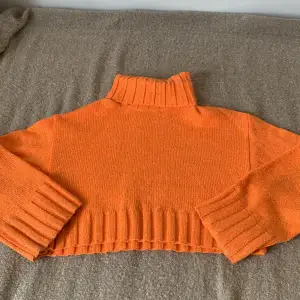 En orange stickad polotröja från H&M Divided. Tröjan har långa ärmar och ribbstickade muddar vid ärmslut, nederkant och krage. Den är i storlek S.