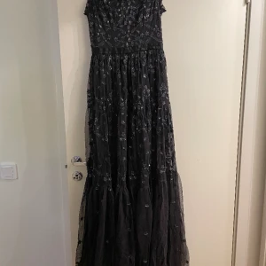Svart klänning - Svart klänning med tyll och blommigt mönster från Needle & Thread, storlek 36. Använd en gång så i mycket bra skick.  Se bilder för mått. Omfång vid det svarta bandet (över midjan): 71 cm   Nuddar golvet för mig som är 172 cm lång.