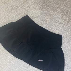 Kjol från Nike i träningsmaterial med inbyggda shorts. Första bilden är kjolen framifrån och den tredje bilden är bakifrån. Stl S