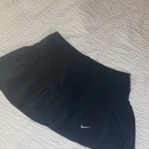 Träningskjol Nike - Kjol från Nike i träningsmaterial med inbyggda shorts. Första bilden är kjolen framifrån och den tredje bilden är bakifrån. Stl S