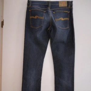 Mörkblå Nudie jeans, Tube Kelly, i NYskick. 29 midja, 34 längd. - Mörkblå Nudie jeans, "Tube Kelly", indigo blue, i NYskick. Raka ben/straight leg/stuprör, låg/normal (?) midja. En del stretch i tyget. 4 fickor. Helt felfria. 29 midja, 34 längd. Helt felfria.  Fler bilder finns om önskas.