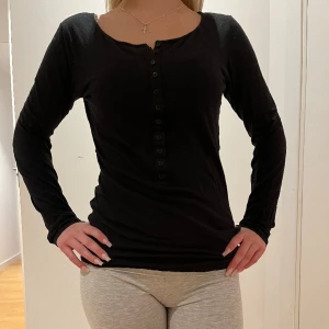 Svart långärmad tröja - Säljer min svarta, långärmade tröja med några knappar som sitter supersnyggt och ger fin form💗den har även två hål längst ut vid ärmarna för tummarna.