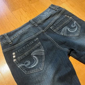 Jane Norman lågmidjade bootcut vintage jeans - Super fina och unika jeans i en marinblå färg med otroligt mycket detaljer både fram, bak, och på knapparna! Säljer för att dem är lite för stora, dem är i jätte bra kvalitet. Fråga om du vill ha mått eller fler bilder 💕💕