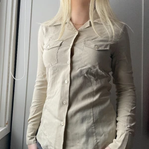 Beige skjorta - Jag säljer nu denna jättefina skjorta eftersom den inte längre passar mig. Den är köpt secondhand men är i så fint skick då jag bara använt den en gång. Skjortan säljs inte längre så den är från en väldigt gammal kollektion, vet inte hur gammal. Jättefin!