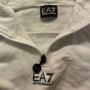 Armani EA7 hoodie - En snygg och sportig vit Armani hoodie med halv zip. HELT NY den är från JD fick i julklapp och har aldrig använt den. Storlek S sitter perfekt på mig som vanligtvis har storlek XS/S💞