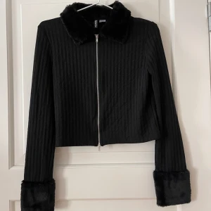 Tröja med fakepäls - Ribbad tröja med dragkedja och fake päls på kragen och ärmarna från H&M i storlek M. Stretchigt material. Använd en gång, i fint skick, Bara att fråga om det är något du undrar! Kan mötas på Järntorget i Göteborg eller skicka, köparen står för frakt.