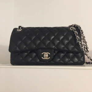 Väska  - Fin svart väska i läder och med silver axelrem !  Flera fack invändigt och ett på baksidan . Helt ny väska i super kvalitet. 