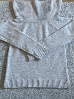 Ljusbeige off shoulder stickad tröja från Gina - Trendig ljusbeige stickad tröja med bred ribbad kant som kan bäras off shoulder. Mjuk och fluffig känsla, långa ärmar och ribbade muddar vid ärmslut och nederkant. Perfekt för dig som vill ha en stilren och mysig look.