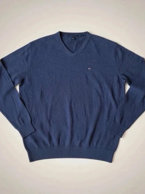 Mörkblå stickad tröja Tommy Hilfiger - Klassisk mörkblå stickad tröja från Tommy Hilfiger i 100% bomull. Tröjan har V-ringning, långa ärmar och en liten broderad logga på bröstet. Ribbstickade muddar vid ärmslut och nederkant ger en snygg passform.