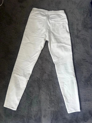 Vita skinny jeans med hög midja - Snygga vita skinny jeans med hög midja och klassiska fem fickor. Jeansen har smal passform och är tillverkade i ett stretchigt material för extra komfort. Perfekta att matcha med en crop top eller hoodie.