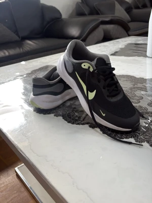 Svarta och vita Nike sneakers - Snygga sneakers från Nike i svart och vitt med limegröna detaljer och swoosh på sidan. Ovandelen är i mesh och syntetmaterial för bra andningsförmåga. Yttersulan har ett mönster för extra grepp och komfort. Klassisk låg modell med svarta skosnören.