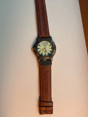 Camel Trophy klocka med brunt läderband - Cool klocka från Camel Trophy med robust boett i metall och brunt läderarmband med Camel Trophy-logga. Urtavlan är ljus och har självlysande visare och index, perfekt för att se tiden i mörker. Klockan har en sportig och äventyrlig look.
