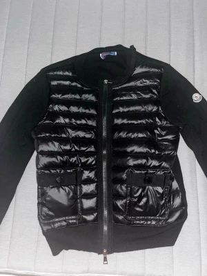 Svart cardiganjacka från Moncler - Snygg svart cardiganjacka från Moncler med quiltad framsida i glansigt material och stickade ärmar. Är använd lite men inte några synliga defekter. Sitter som en S