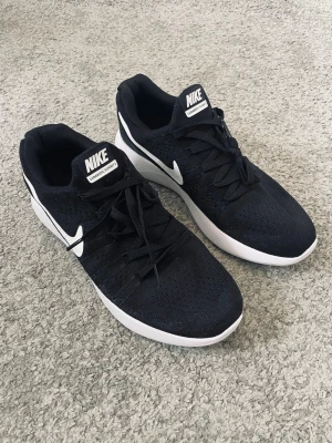 Svarta Nike LunarEpic Flyknit 2 Sneakers - Snygga svarta Nike LunarEpic sneakers med vit sula och klassisk vit swoosh på sidan. Ovandelen är i ventilerande meshmaterial och skorna har snörning för perfekt passform. Perfekta för dig som gillar stilrena och sportiga sneakers.