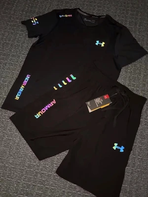 Svart träningsset från Under Armour - Säljer ett par svart träningsset från Under Armour med regnbågsfärgad logga och textdetaljer. Shortsen har snörning i midjan och är perfekta för träning eller chill. Materialet känns lätt och andas bra. Storlek S, helt ny 