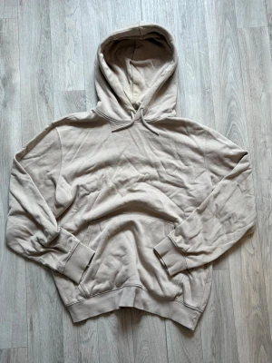 Beige hoodie från Weekday - Säljer en beige hoodie från Weekday i storlek S. Hoodien har en klassisk huva med dragsko, ribbade muddar vid ärmar och nederkant samt en stor magficka. Tillverkad i mjukt bomullsmaterial som känns skönt mot huden. Perfekt för en avslappnad och stilren look.