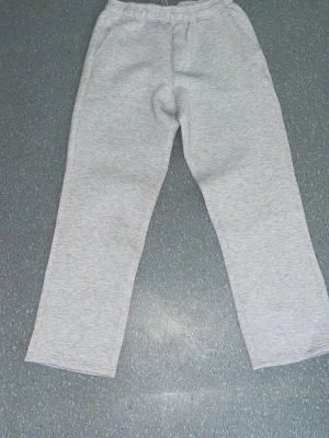 Ljusgrå mjukisbyxor med resårmidja - Säljer ett par ljusgrå mjukisbyxor med resår i midjan och raka ben. Byxorna har en bakficka och är gjorda i mjukt sweatshirtmaterial, perfekta för chill dagar. Klassisk och enkel design som passar till det mesta.