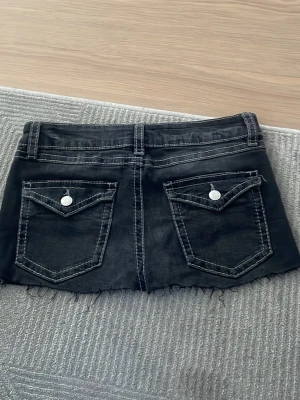 Svart jeanskjol - Säljer en svart kort jeanskjol med rå, fransig kant. Har sytt om de lite eftersom de var jeans innan. Midjemått: 38cm, Längd: 26cm.
