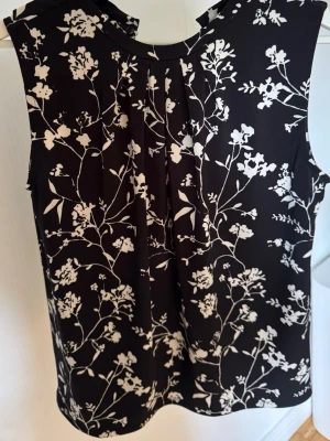 Svart blommig ärmlös blus från STOCKH LM - Snygg svart ärmlös blus från STOCKH LM med vitt blommigt mönster. Blusen har rund halsringning och mjukt, lätt material som faller fint. 