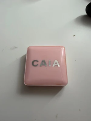 CAIA rosa puderrouge - Säljer ett puderrouge från CAIA i en snygg rosa nyans. Kommer i en stilren, ljusrosa fyrkantig dosa med spegel och silvrig logga på locket. Rouget har en rund, vågig yta och ger ett fräscht glow till kinderna.