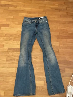 Blå bootcut jeans med låg midja - Säljer ett par blå bootcut jeans med låg midja och slitningar på låren för en cool vintage-look. De är i otroligt bra skick och knappt använda, de är i storlek xs 32 men passar för mig som har s 36 så de är lite stora i storleken men är på gränsen att passa mig då de är lite för små. Köpte dessa för 600kr och är knappt använda