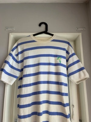 Randig t-shirt med svampbroderi - Vit och blå randig t-shirt med korta ärmar och ett broderat svampmotiv på bröstet från Zara. T-shirten har en avslappnad passform och är gjord i ett mjukt bomullsmaterial. Perfekt för dig som gillar unika detaljer och sköna plagg.
