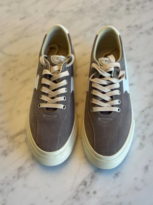 Gråa sneakers med vit sula, Stepney Workers Club - Snygga sneakers i grå mocka med vit platåsula och vita detaljer på sidan från SWC (Stepney Workers Club). Skorna har vita snören och en klassisk låg siluett som passar till många olika stilar. Perfekta för dig som gillar en clean och stilren look. Oanvönda. Nypris 1800 SEK. 