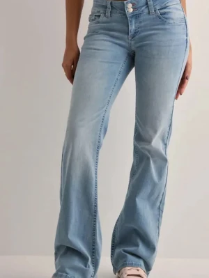 Ljusblå bootcut jeans med brodyr - Säljer ett par ljusblå bootcut jeans med snygg broderad detalj i rosa på bakfickorna. Jeansen har hög midja, klassisk femficksdesign och stängs med knapp och dragkedja. Perfekta för dig som gillar en avslappnad men trendig look. Jensen är även lågmidjade.
