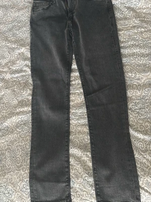 Svarta Levi jeans - Säljer ett par svarta jeans med rak passform och klassisk femficksdesign. Jeansen har normal midja och dragkedja i gylfen. Materialet är denim som ger en tidlös look och passar till det mesta. Perfekta för dig som gillar en enkel och clean stil.