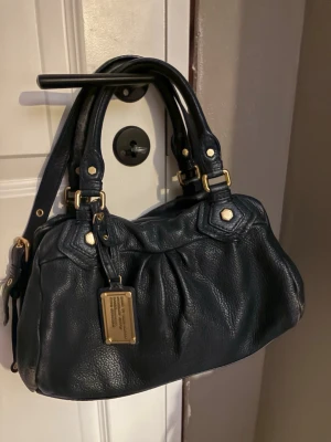 Mörkblå marc Jacobs väska med gulddetaljer - Jätte snygg Marc Jacobs väska i bra skick. Lite små deffekter på lädret annars är det inget annat.