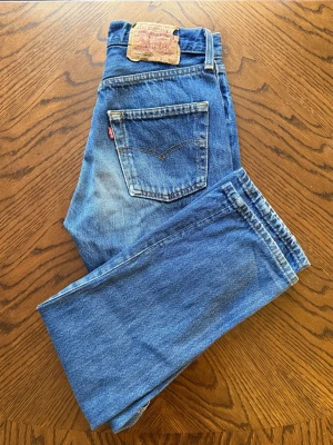 Vintage Levi's 501 made in usa Jan 1994) | Grym Blå Tvätt & Straight Fit - Helt otroliga vintage Levi's 501 Original tillverkade i USA (januari 1994, fabrikskod 524). Kraftig och rejäl 100% bomullsdenim med klassisk knappgylf, helröd tab, intakt läderpatch och en helt magisk, naturlig fade/slitning över låren och bakfickorna.  Perfekt, tidlös unisex-modell som ger den helt rätta retro-silhuetten. Toppskick i hela tyget!Lappen säger W28 L32 men de har krympt naturligt med åren och sitter som en modern W26/W27 L30. (Mått Midja 33,5cm Innerben 74,5cm Fotvid 19cm)