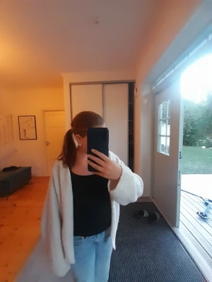 Vit fluffig kofta med vida ärmar - Mysig, oversized vit kofta i fluffigt material. Koftan har långa, vida ärmar och en öppen front utan knappar. Perfekt att slänga över en topp för en avslappnad look. Passar dig som gillar en chill och enkel stil.