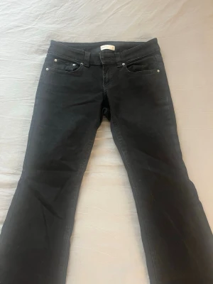 Svarta bootcut jeans med fickdetaljer - Snygga svarta jeans med bootcut-modell och silverfärgade nitar. Jeansen har klassiska fem fickor, varav bakfickorna har lock och knapp. Tillverkade i ett mjukt denimtyg som sitter skönt och passar till många olika stilar.