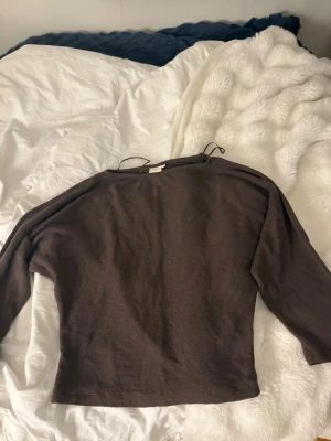 Brun långärmad tröja med snörning - Mysig brun långärmad tröja med avslappnad passform och snörningsdetaljer vid halsen. Perfekt till jeans eller kjol för en enkel och stilren look. Tillverkad i mjukt material som känns skönt mot huden.