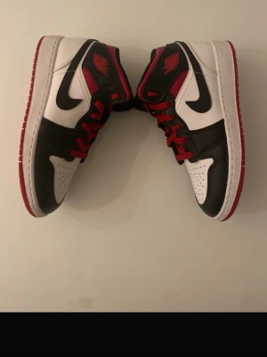 Svarta, vita och röda sneakers - Snygga sneakers i svart, vitt och rött med klassisk design och kontrasterande färgblock. Skorna har röda skosnören, svart swoosh på sidan och röd yttersula. Tillverkade i läder med perforerad tåbox för extra ventilation.