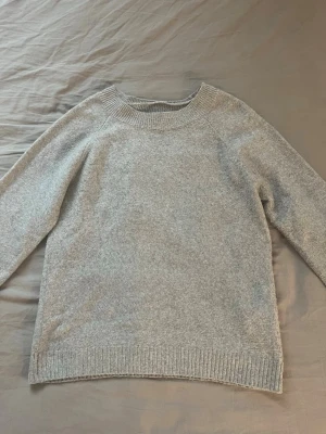 Ljusgrå stickad tröja - Mysig ljusgrå stickad tröja med rund halsringning och ribbade muddar vid ärmslut och nederkant. Tröjan har en enkel och stilren design, perfekt för lager på lager och passar till det mesta.