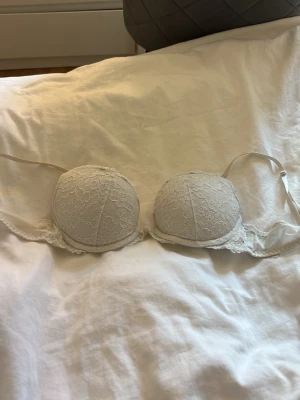 Vit spets-bh med vadderade kupor - Snygg vit bh med vadderade kupor och spetsdetaljer över hela framsidan. Axelbanden är justerbara och bh:n har bygel för extra stöd. Perfekt för dig som gillar en feminin och klassisk stil.
