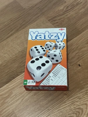 Yatzy tärningsspel från Tactic - Yatzy är ett klassiskt tärningsspel från Tactic med fem vita tärningar och poängblock. Förpackningen är orange och vit med stora tärningar på framsidan. Perfekt för spelkvällar med vänner eller familj.
