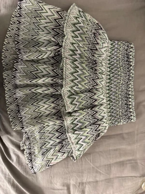 Kort kjol med zigzag-mönster - Säljer en kort kjol med volanger och elastisk midja. Kjolen har ett coolt zigzag-mönster i svart, vitt och grönt. Perfekt för dig som gillar att sticka ut med mönster och vill ha en bekväm men trendig look.