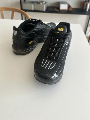 Nike Air Max Plus Tn Svart sneaker - Snygga svarta Nike Air Max Plus Tn sneakers med reflekterande detaljer och synlig Air-dämpning i sulan. Ovandelen är i mesh och syntet med vita och silverfärgade linjer. Klassisk Tn-logga på plösen och hälen. Perfekta för dig som gillar streetwear och sportig stil.