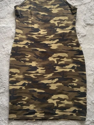 Camo tight klänning i polyester - Säljer en klänning med camouflagemönster i gröna och bruna toner. Klänningen är ärmlös och gjord i stretchigt material, 95% polyester och 5% elastan. Perfekt för dig som gillar streetwear och vill sticka ut med en edgy look.