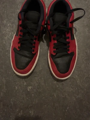 Svarta och röda Nike sneakers - Säljer ett par snygga Nike sneakers i svart och rött med klassisk swoosh på sidan. Skorna har lågt skaft, svarta skosnören och vit sula. Ovandelen är i läder och designen är riktigt clean och tidlös.