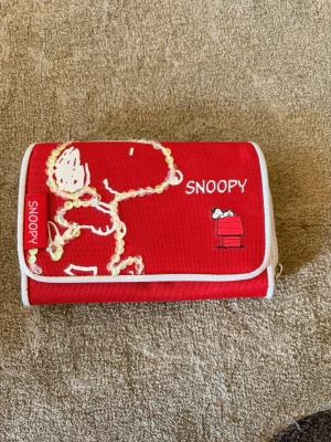 Röd Snoopy plånbok  - Cool röd plånbok med Snoopy-tryck och vita detaljer. Stängs med tryckknapp och har vit kant runtom. Knappt använd 