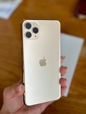 Guldig iPhone 11 Pro Max - Snygg guldig iPhone med stilren design och trippelkamera på baksidan. Mobilen har rundade kanter och glasbaksida med Apple-loggan i mitten. Perfekt för dig som gillar både funktion och utseende.