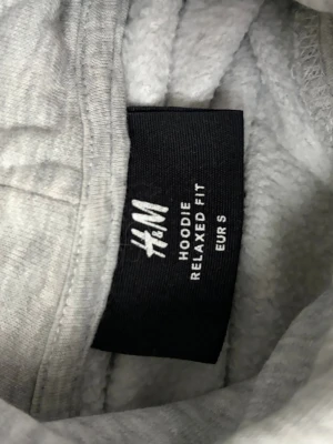 Ljusgrå hoodie från H&M - En stilren ljusgrå hoodie från H&M i relaxed fit. Hoodien har huva och en stor magficka framtill. Tillverkad i mjukt material som känns skönt mot huden. Perfekt för en avslappnad och trendig look.