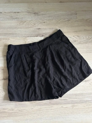 Svarta loose shorts med fickor - Svarta shorts med lös passform och praktiska fickor på sidorna. De har en enkel design med lätt rynk vid midjan och är tillverkade i ett mjukt tyg som känns bekvämt mot huden. Perfekta för varma dagar och enkel att matcha med olika toppar.