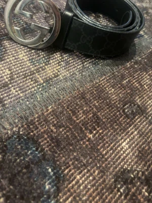 Svart skärp med silver GG-spänne Gucci - Snyggt svart skärp från Gucci med klassiskt GG-mönster och stort silverfärgat GG-spänne. Skärpet är gjort i skinn och har en stilren look som passar till många outfits. Perfekt accessoar för dig som gillar exklusiva detaljer.